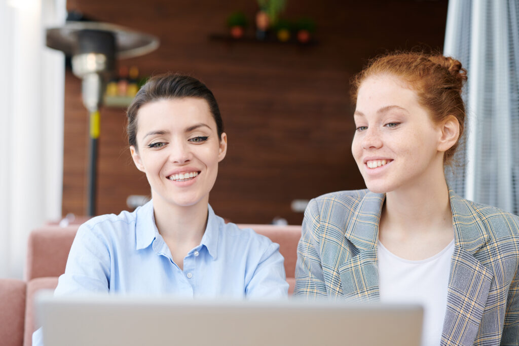 Zwei Frauen sitzen vor Laptop und lächeln