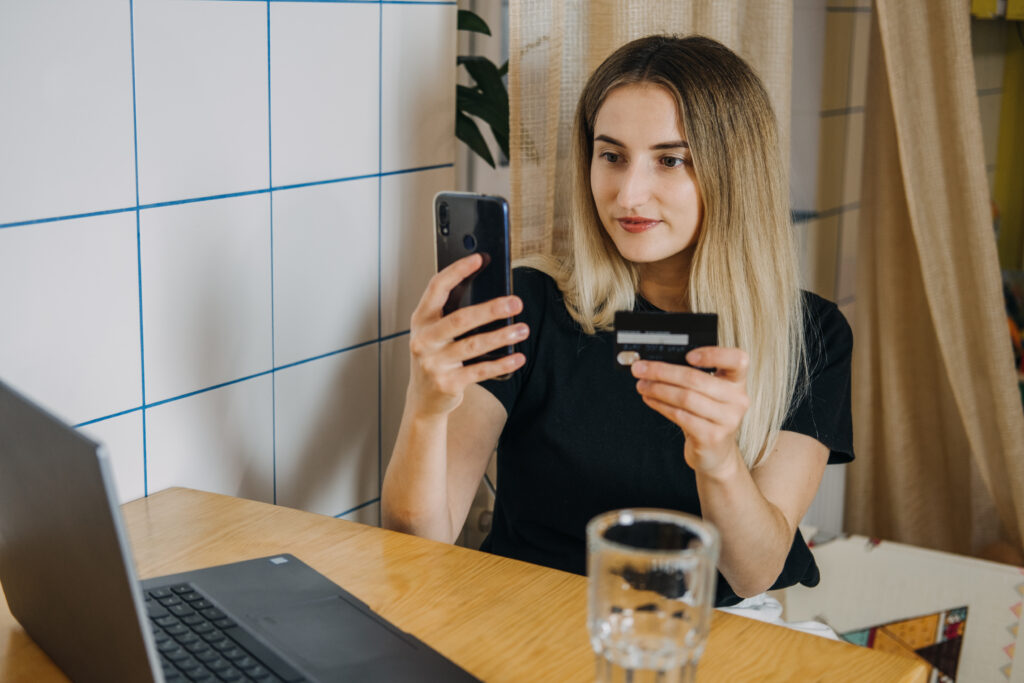 Frau hält Handy in der Hand und sitzt vor Laptop