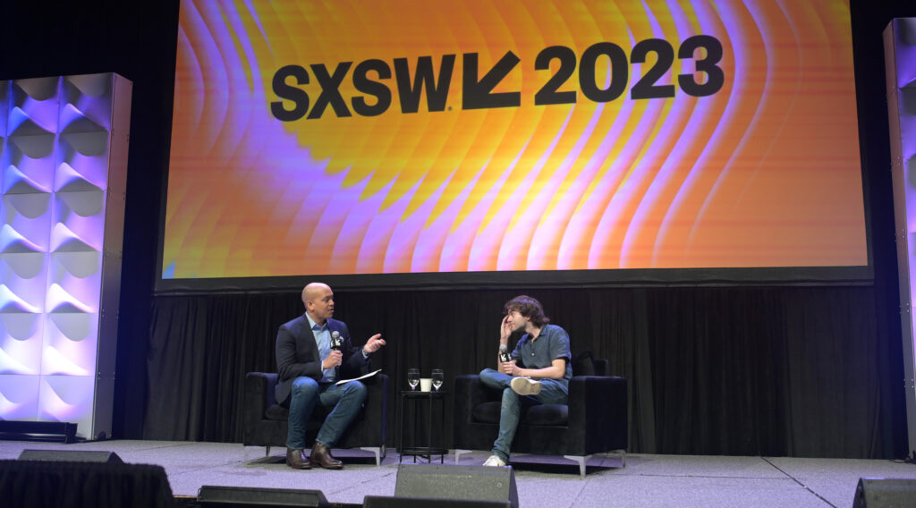 Boyan Slat sitz auf der Bühne und wird von einem Mann mit Mikrofon befragt. Dahinter das riesige Schild SXSW 2023
