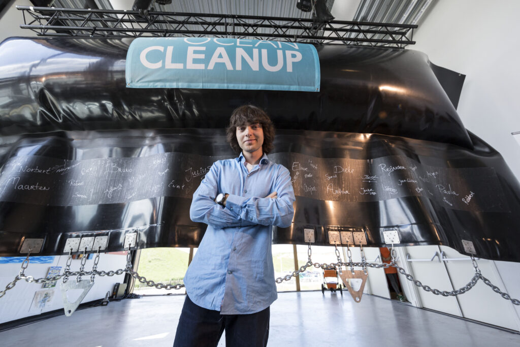 Boyan Slat steht mit verschränkten Armen vor dem Schild Cleanup