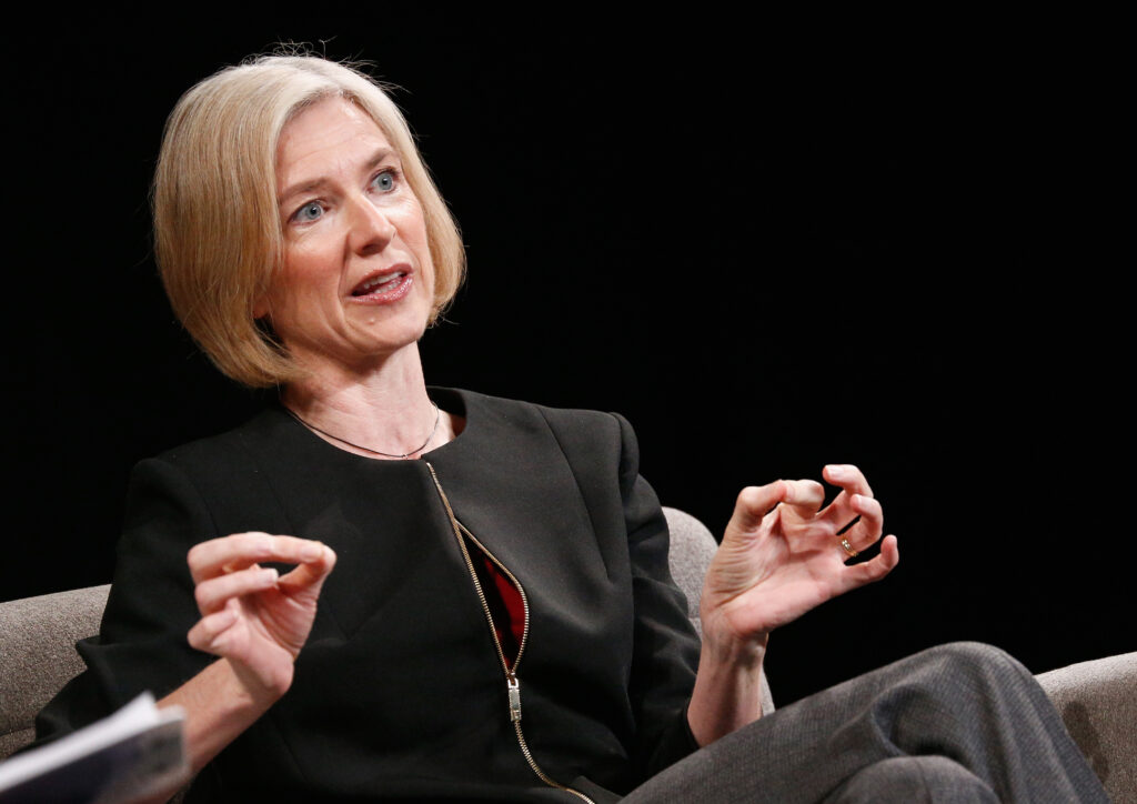 Jennifer Doudna in schwarzer Kleidung blickt seitlich in die Kamera und hält in beiden Händen Daumen und Zeigefinger zusammen