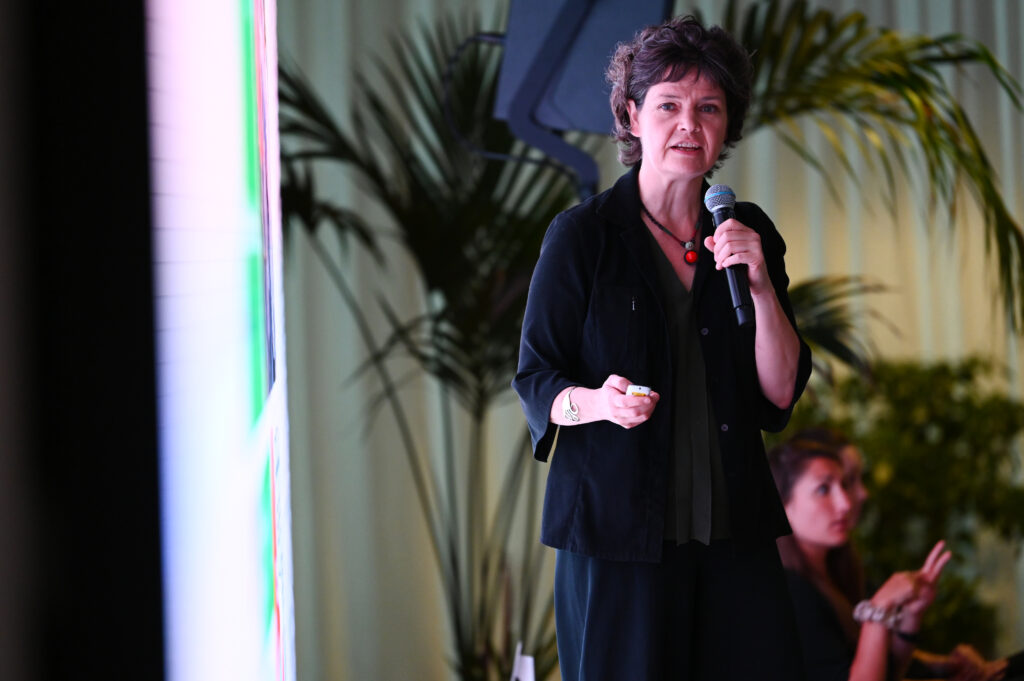 Kate Raworth mit einem Mikrofon in der Hand. Dahinter eine Palme