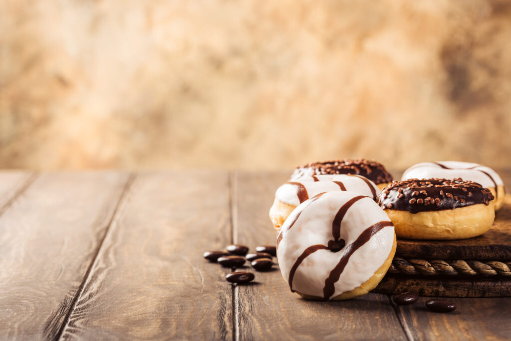 Fünf Schokodonuts mit weißer und brauner Glasur liegen auf einem Teller auf einem Holztisch. 