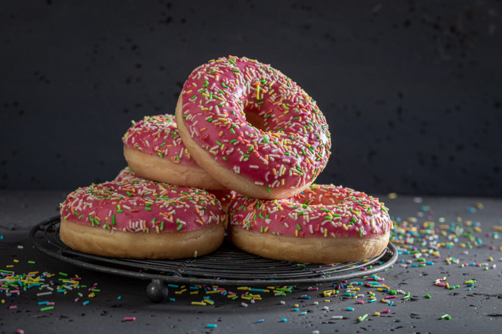 Vier Donuts mit rosa Zuckerglasur und buntem Streusel auf einer Platte auf einem Tisch