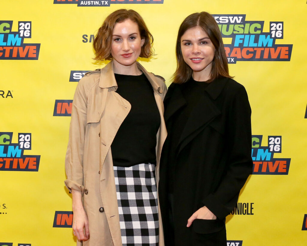 Emily Weiss steht neben einer Frau vor einem Plakat