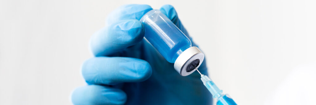 Blauer Hygienehandschuh und eine kleine Flasche, in der eine Spritze gesteckt wird