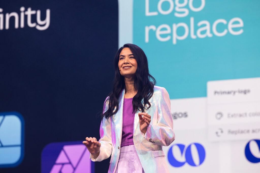 Melanie Perkins steht mit rosa Hosenanzug auf einer Bühne