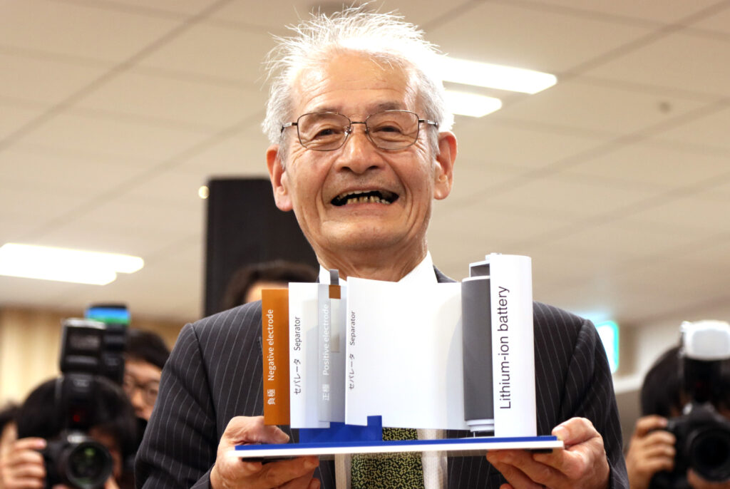 Akira Yoshino hält vier Bücher und lacht über das ganze Gesicht