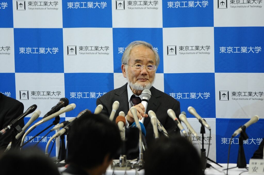 Yoshinori Ohsumi sitzt vor zahlreichen Mikrofonen