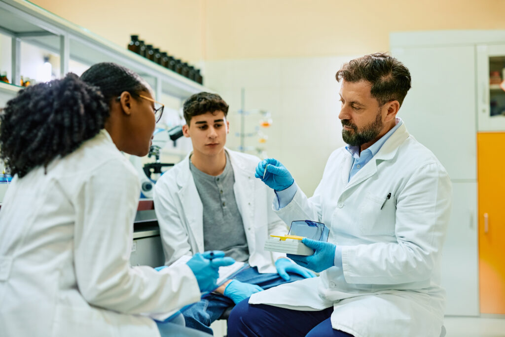 Drei Wissenschaftler sitzen zusammen und schauen auf eine Pipette